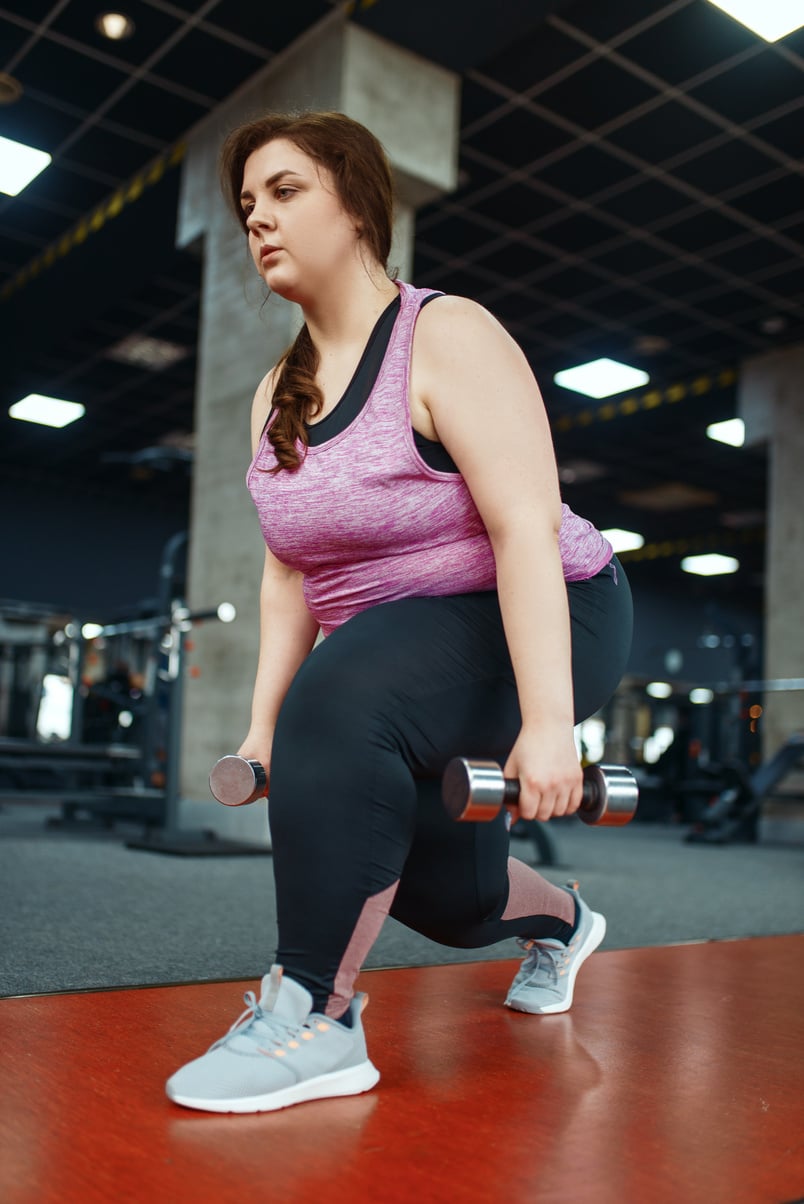 Overweight Woman Exercising with Dumbbells in Gym
